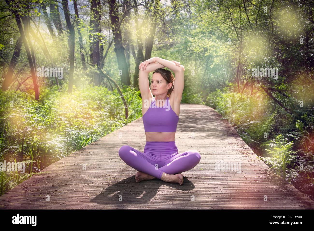 Eine Frau, die Yoga oder Pilates praktiziert und auf einer Holzpromenade im Wald sitzt. Sport-, Dehn- und Flexibilitätsübungen Stockfoto