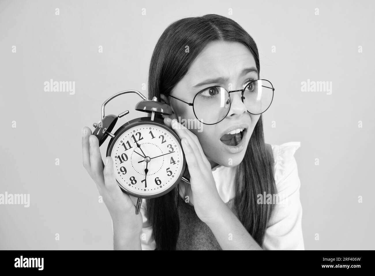 Überrascht lustige Teenager Mädchen Kind halten Uhr isoliert auf gelben Studio-Hintergrund. Teenager-Kind mit Wecker, der die Zeit anzeigt. Stockfoto