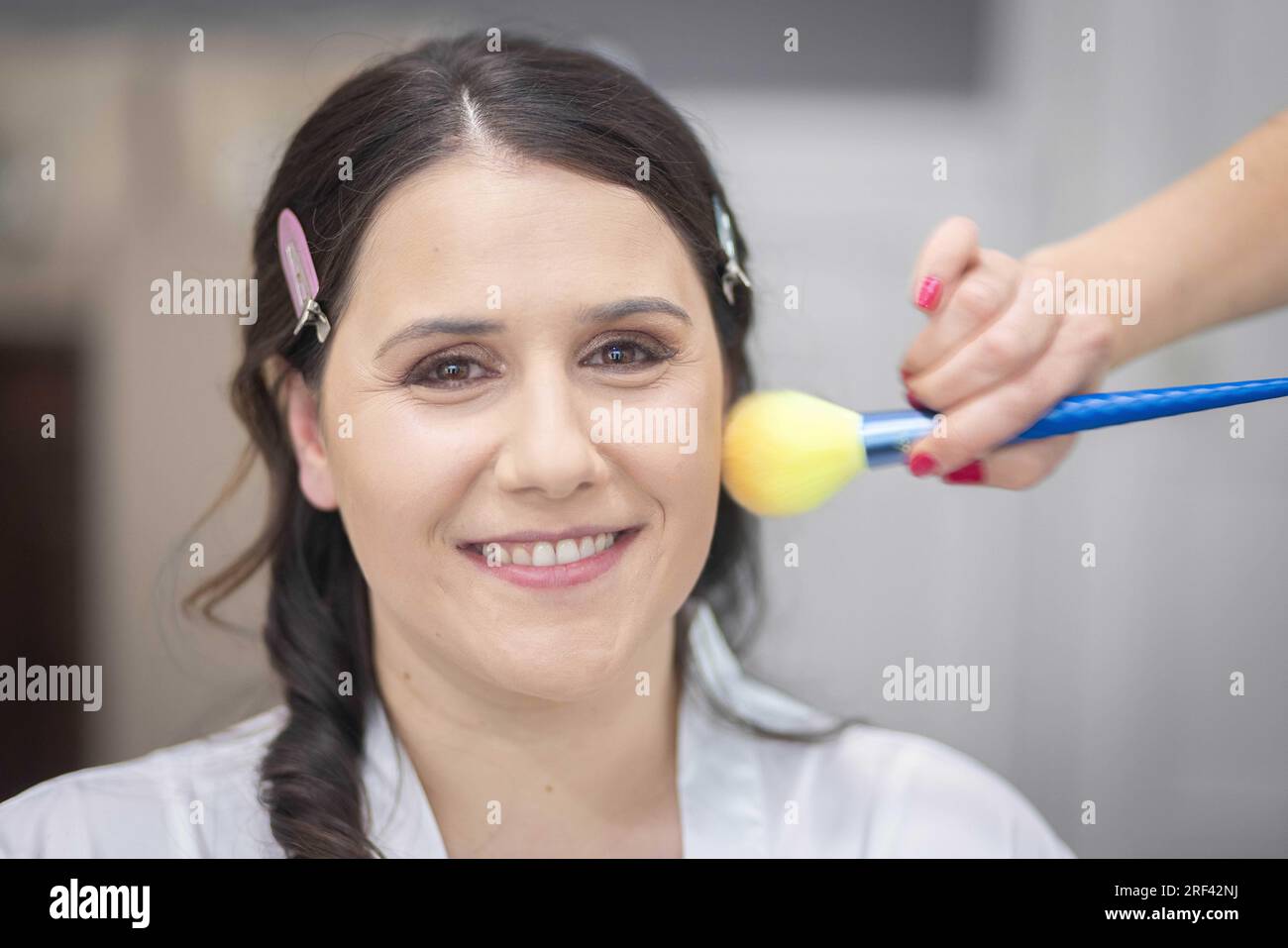 Nahaufnahme der Make-up-Bürste, die Puder auf die lächelnde Braut aufträgt, um am Morgen ihrer Hochzeit zu sein Stockfoto
