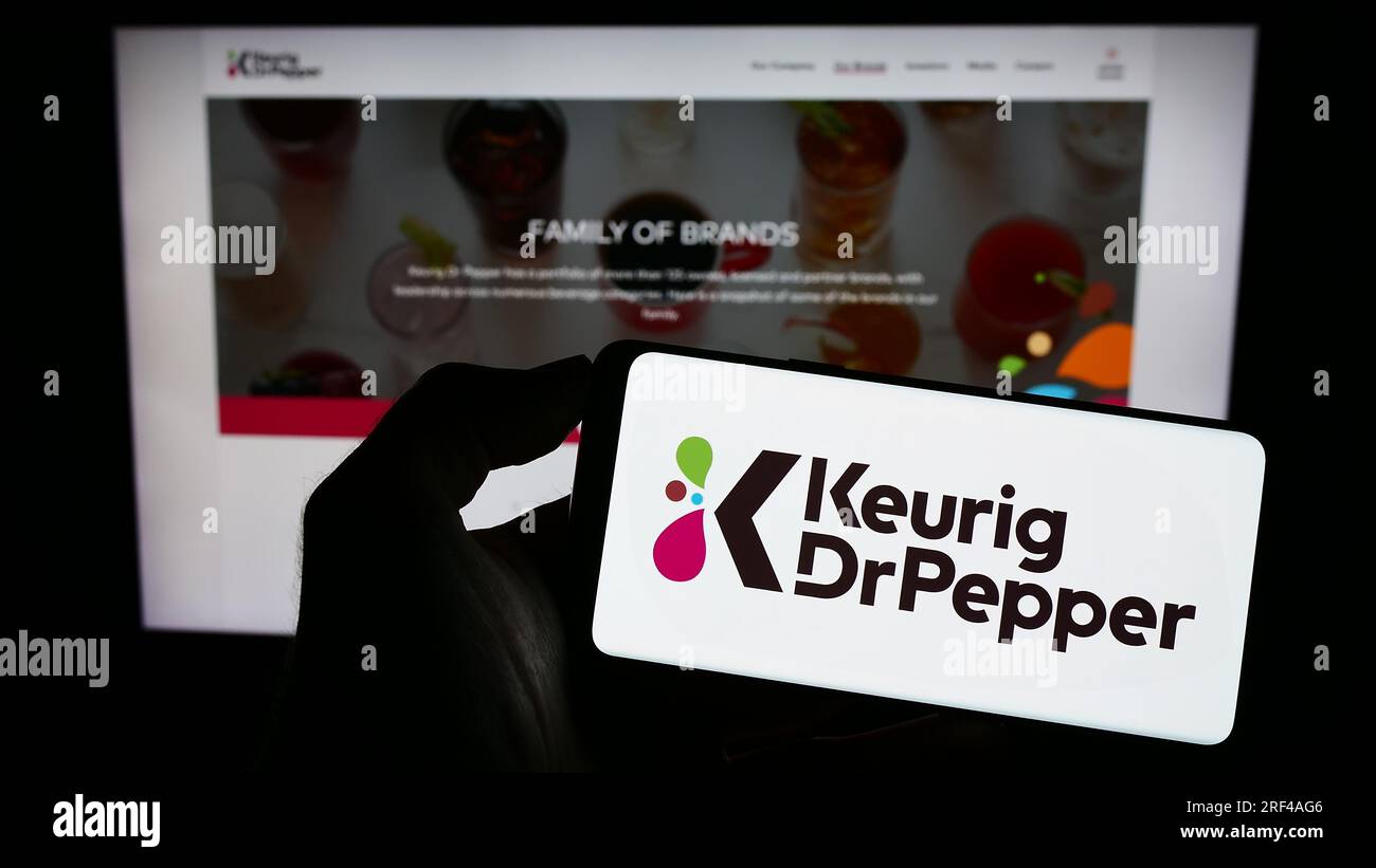 Person, die ein Mobiltelefon mit dem Logo des amerikanischen Getränkeherstellers Keurig Dr. Pepper Inc. Auf dem Bildschirm vor der Webseite hält. Konzentrieren Sie sich auf das Display des Telefons. Stockfoto