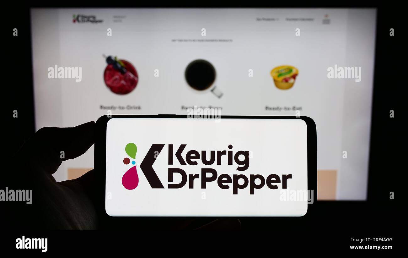 Person, die ein Mobiltelefon mit dem Logo des US-amerikanischen Getränkeherstellers Keurig Dr. Pepper Inc. Auf dem Bildschirm vor der Unternehmenswebseite hält. Konzentrieren Sie sich auf das Display des Telefons. Stockfoto