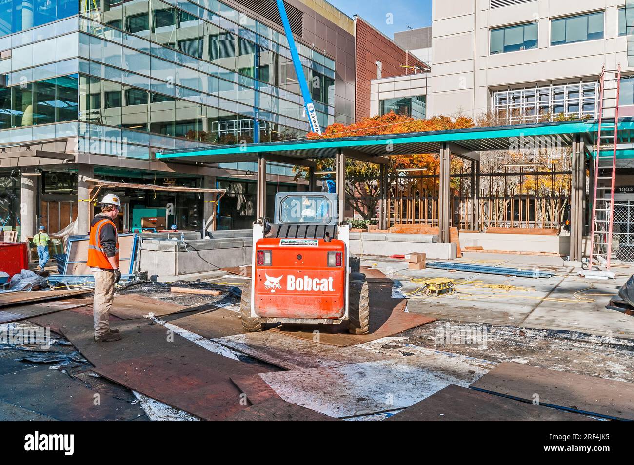 Bauarbeiter auf einer Baustelle für eine Gesundheitseinrichtung. In der Abbildung ist ein Kompaktlader von Bobcat zu sehen. Stockfoto