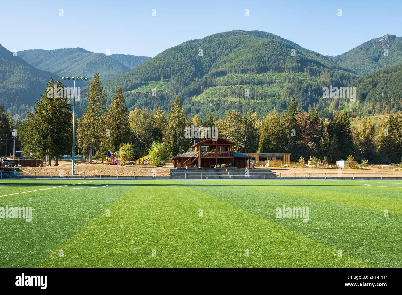 Grünes Gras auf einem Fußballfeld und Wäldern. Fußballfeld auf dem Lande. Berglandschaft in Kanada mit einem Fußballfeld. Natürliche Grasstruktur. Kopien Stockfoto
