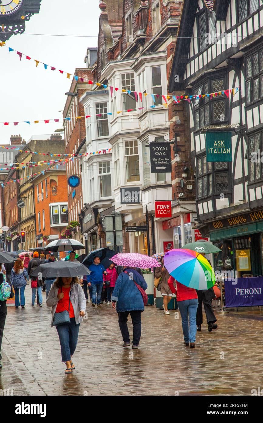 Menschen, die im Regen unter Schirmen in der Hauptstraße Winchester spazieren gehen und einkaufen, während des schrecklichen nassen Sommerwetters in England im Jahr 2023 Stockfoto