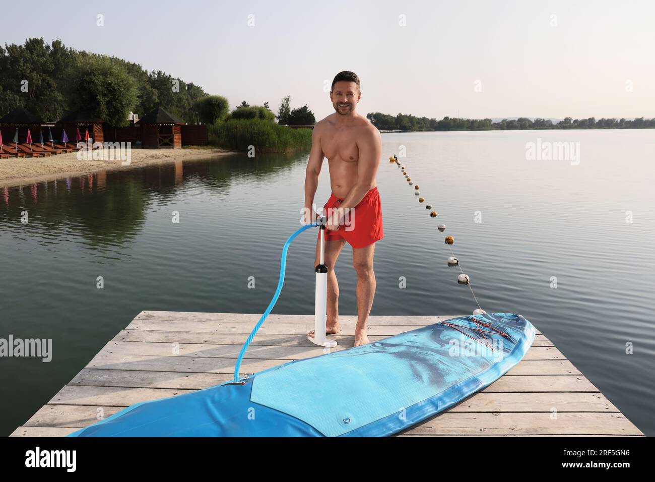 Ein Mann, der das SUP-Brett am Pier hochpumpt Stockfoto