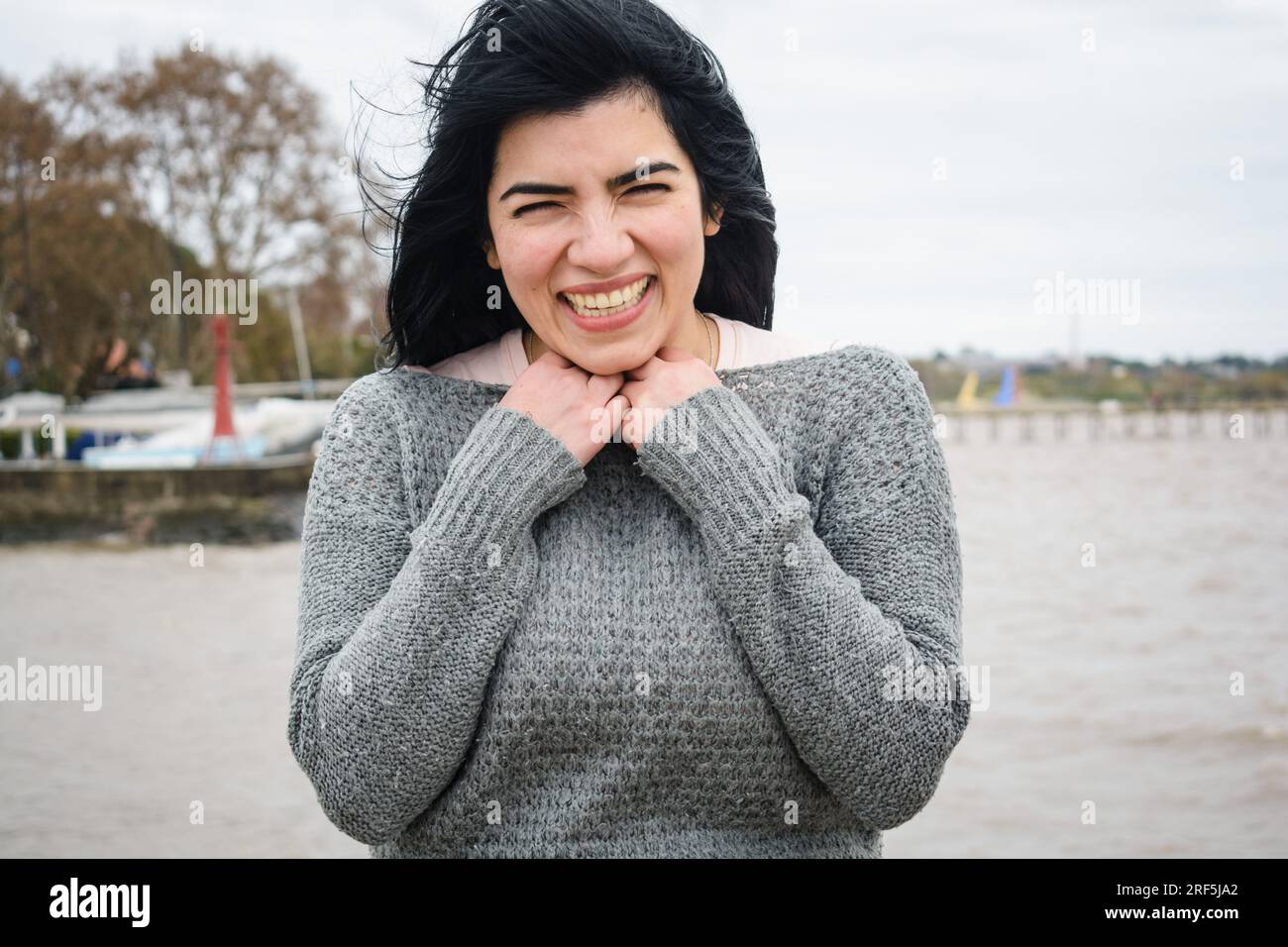 Taille hoch Porträt einer jungen lateinischen Touristin venezolanischer Herkunft in einem grauen Pullover, sie ist kalt und steht glücklich auf dem Pier und schaut sich an Stockfoto