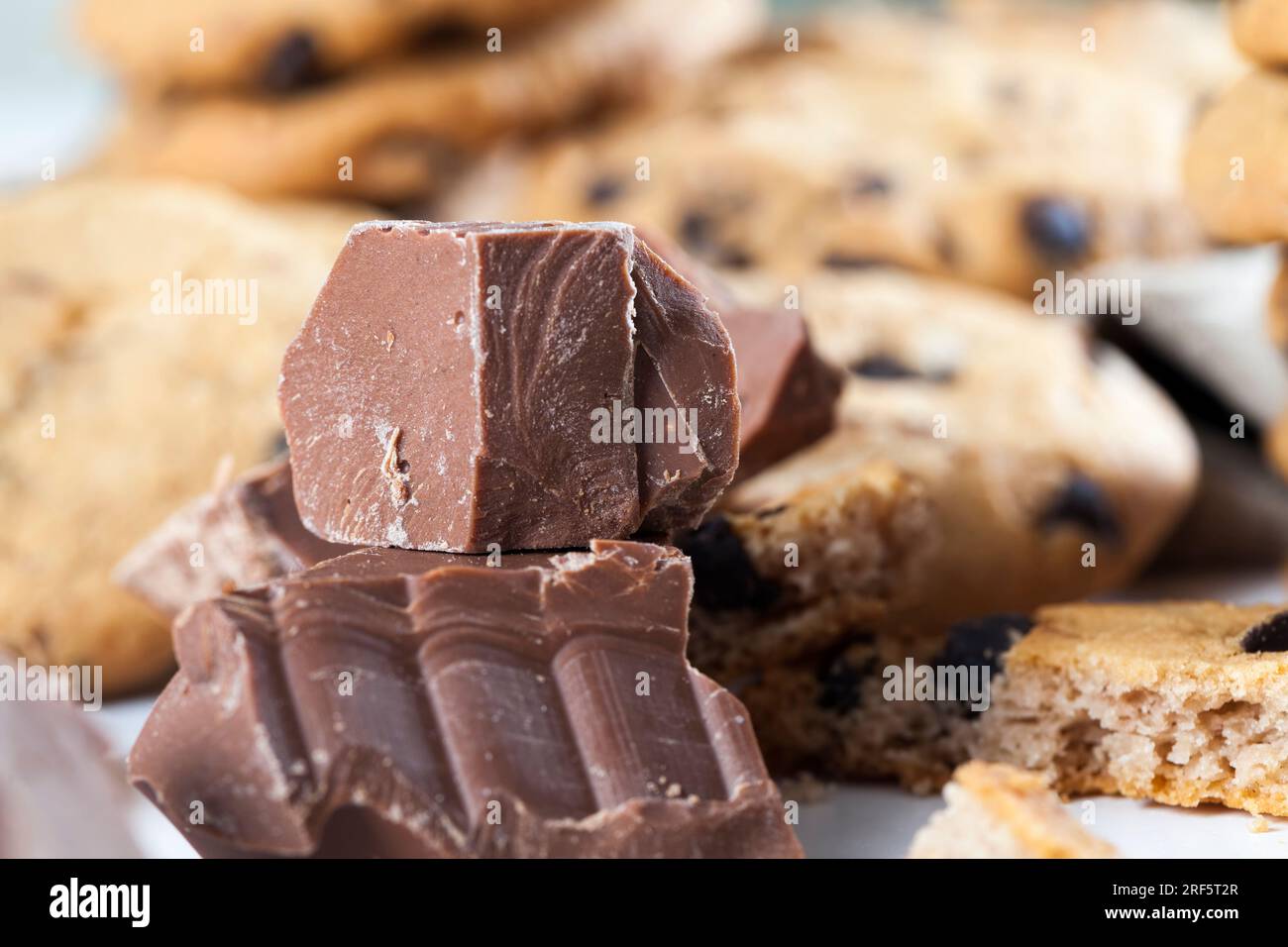 Große Stücke Milchschokolade auf dem Tisch, zerbrochene Schokolade und Weizenkekse mit Schokoladentropfen, Fast Food-Artikel, sehr kalorienreiches Kakaopulver Stockfoto