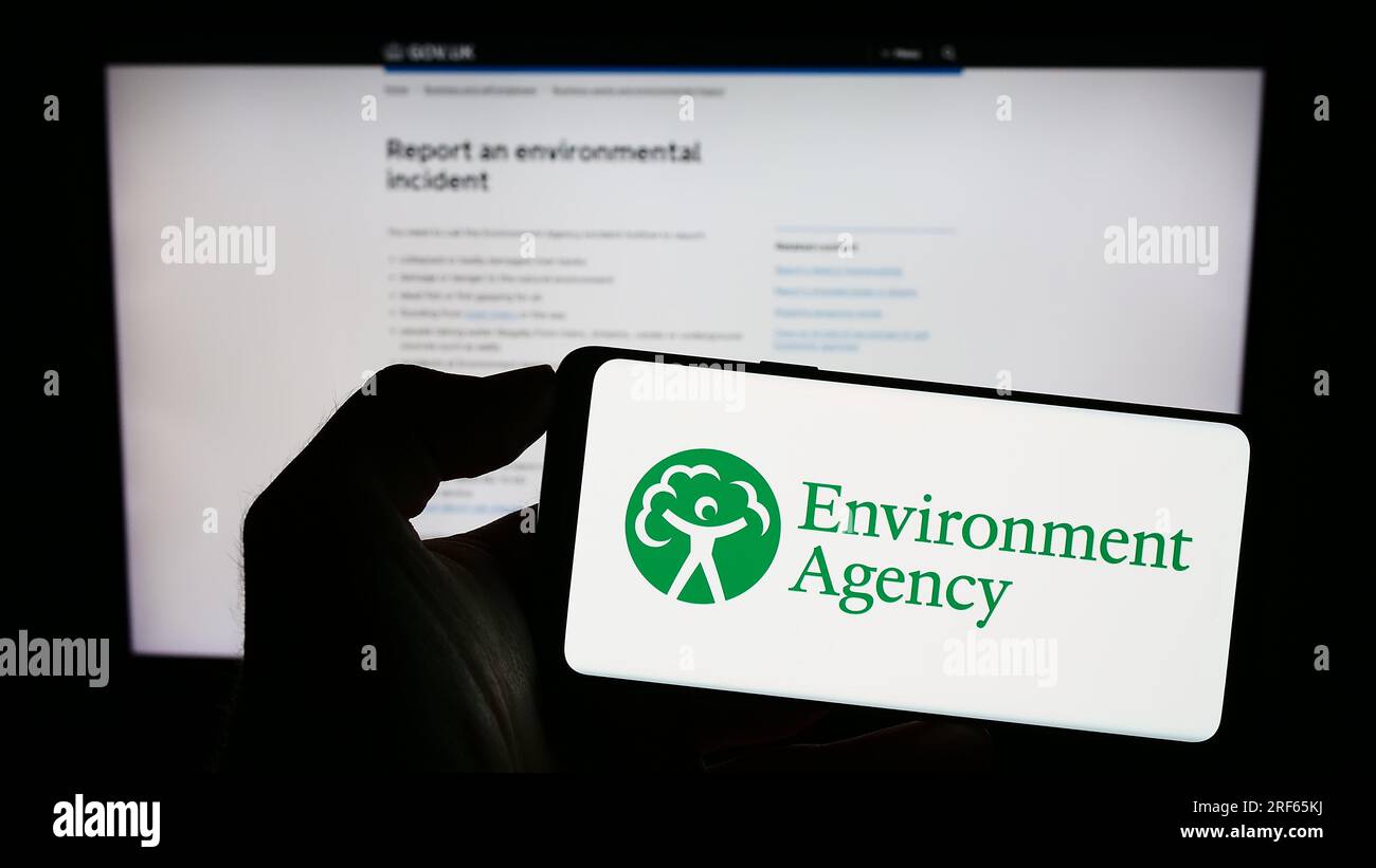 Person, die ein Mobiltelefon mit dem Logo der British Public Body Environment Agency (EA) auf dem Bildschirm vor der Webseite hält. Konzentrieren Sie sich auf das Display des Telefons. Stockfoto