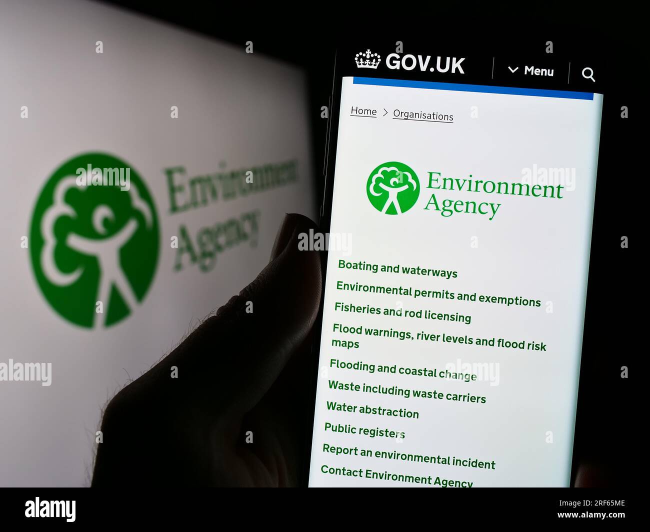 Person, die ein Mobiltelefon mit einer Webseite der British Public Body Environment Agency (EA) auf dem Bildschirm vor dem Logo hält. Konzentrieren Sie sich auf die Mitte des Telefondisplays. Stockfoto