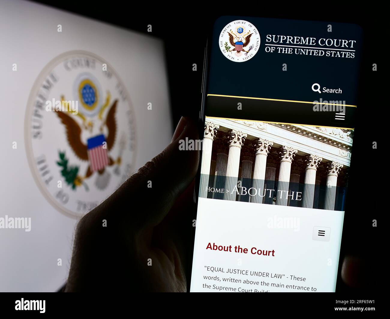 Person, die ein Mobiltelefon mit einer Website der USA besitzt Supreme Court (SCOTUS) auf der Leinwand vor dem Siegel. Konzentrieren Sie sich auf die Mitte des Telefondisplays. Stockfoto