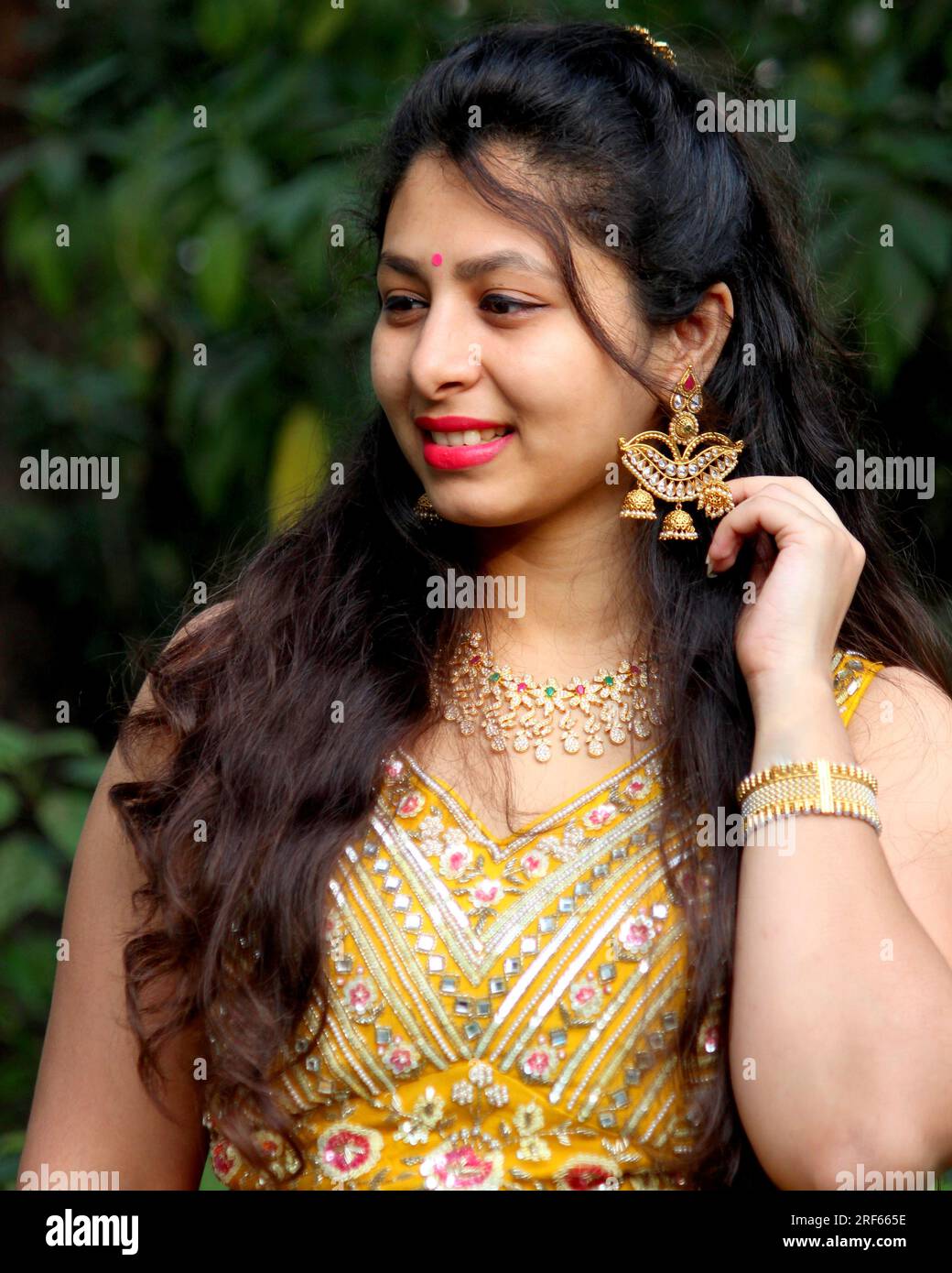 Wunderschöne Frau mit langen lockigen Haaren, trägt gelbe Ghaghra und Chili und Diya-förmige Ohrringe und Schmuck für die indische Hochzeit. Ohrring in Lampenform. Stockfoto