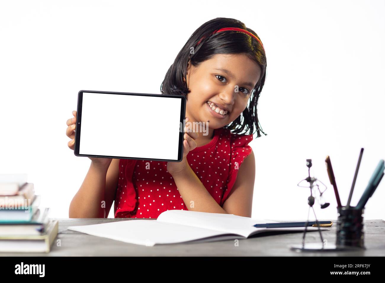 Ein hübsches indisches Mädchen, das studiert und auf dem Tisch auf weißem Hintergrund einen leeren Bildschirm mit Tablet zeigt Stockfoto