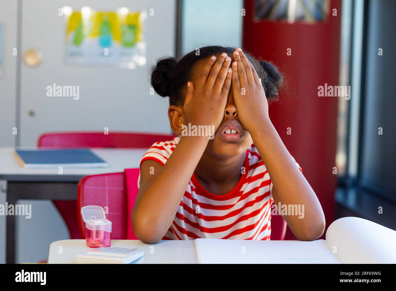 Erschöpftes afroamerikanisches Schulmädchen an der Rezeption und bedeckte ihre Augen mit Händen in der Grundschule Stockfoto