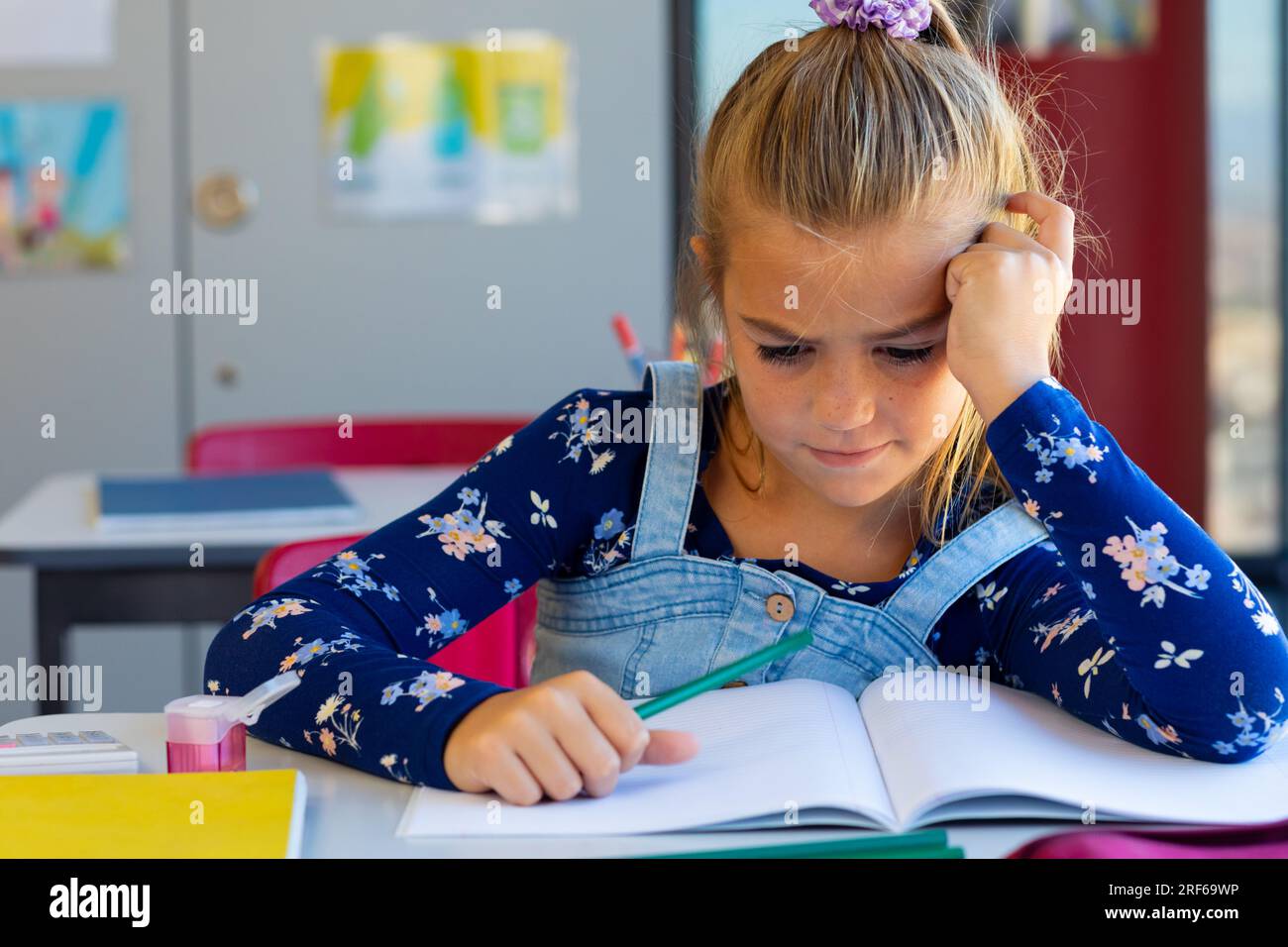Erschöpftes weißes Schulmädchen, das am Schreibtisch sitzt und in der Grundschule lernt Stockfoto