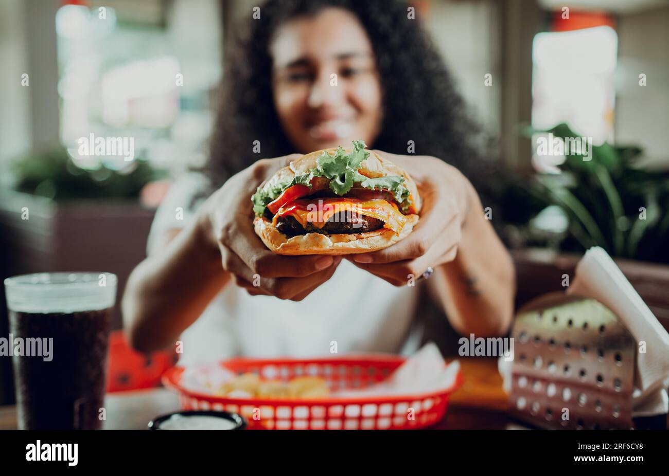 Lächelndes Mädchen, das einen Burger in einem Restaurant zeigt. Nahaufnahme einer Frau, die einen leckeren Hamburger in einem Restaurant zeigt Stockfoto
