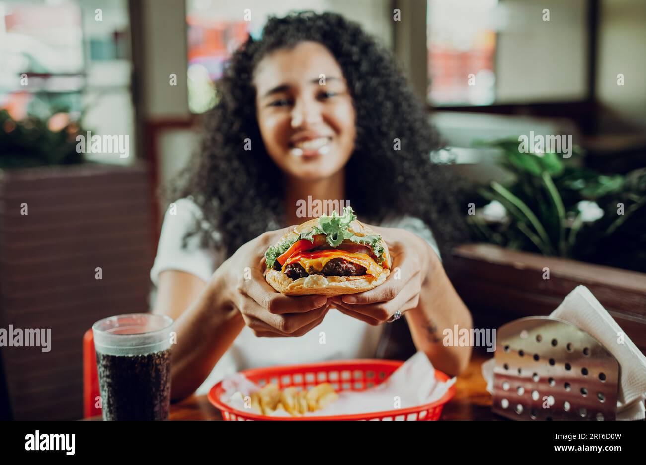 Glückliches Mädchen, das Burger in einem Restaurant zeigt. Nahaufnahme eines Mädchens, das leckere Hamburger in einem Restaurant zeigt Stockfoto