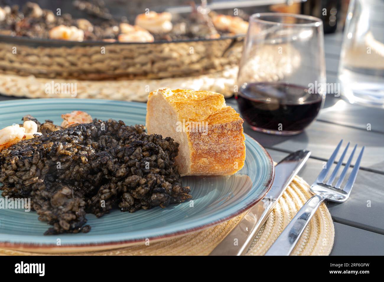 Schwarzer Reis mit Tintenfisch und Garnelen in einer Paella-Pfanne. Fertig zum Essen, mit Brot und Rotwein Stockfoto
