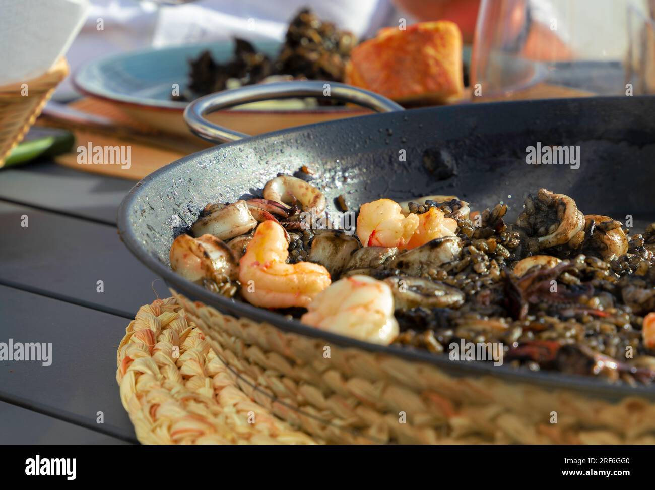 Schwarzer Reis mit Tintenfisch und Garnelen in einer Paella-Pfanne. Fertig zum Essen, mit Brot und Rotwein Stockfoto