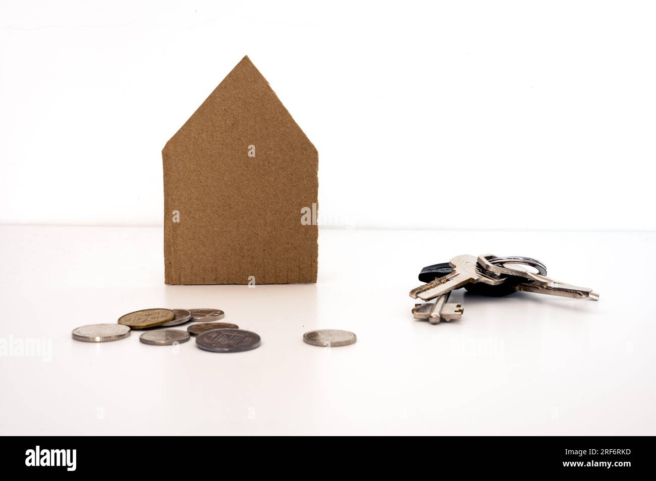 Papphaus mit einem Haufen Schlüssel und Münzen vorne. Hypotheken, Wohnungen, Finanzen, Immobilien, Häuser verkaufen, Verkauf Stockfoto