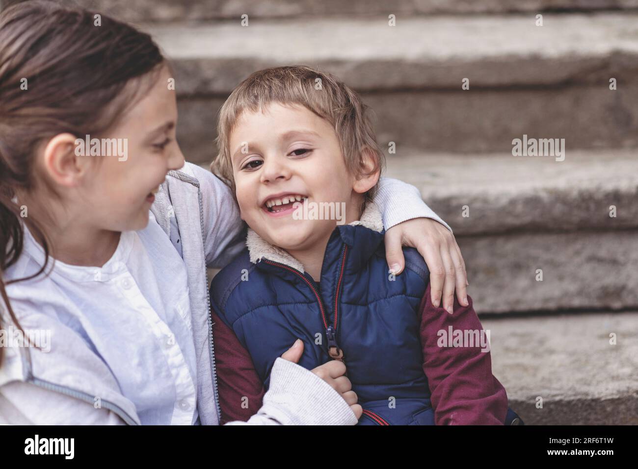 Zwei Kinder sitzen auf der Treppe, Geschwister lieben, ältere Schwester umarmt ihren kleinen Bruder, Glückskonzept, Schwesterliebe Stockfoto