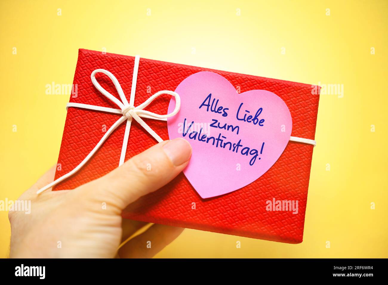 FOTOMONTAGE, Hand hält Geschenk mit einem herzförmigen Zettel und der Aufschrift alles Liebe zum Valentinstag Stockfoto