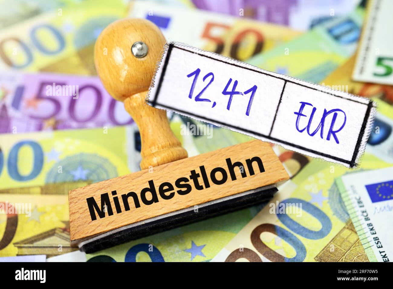 FOTOMONTAGE, Stempel mit Aufschrift Mindestlohn und Zettel mit Aufschrift 12,41 EUR auf Geldscheinen Stockfoto