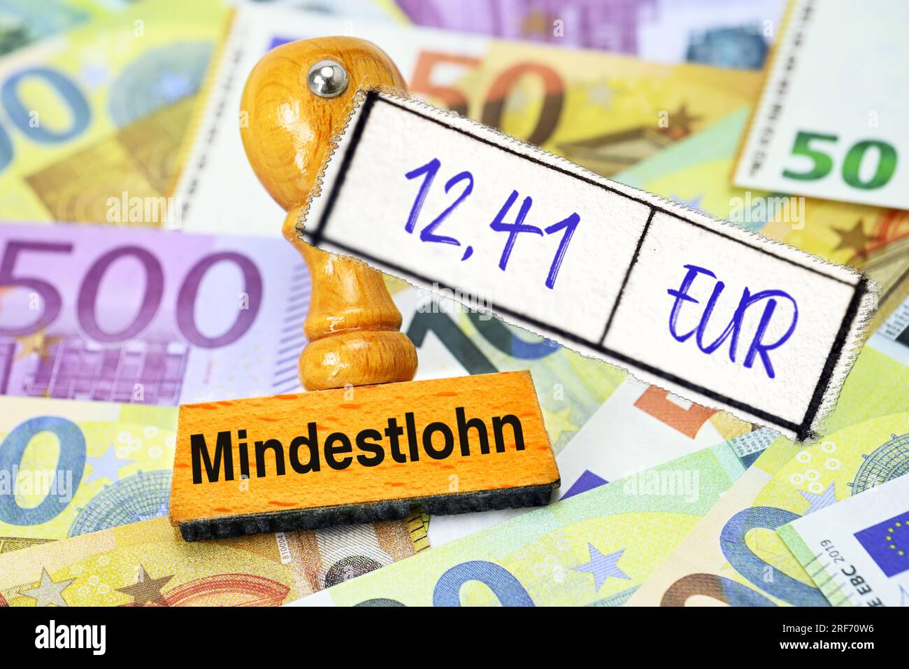FOTOMONTAGE, Stempel mit Aufschrift Mindestlohn und Zettel mit Aufschrift 12,41 EUR auf Geldscheinen Stockfoto