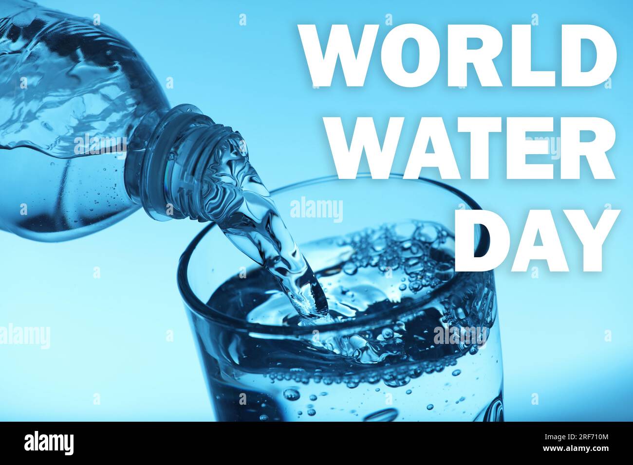 Text World Water Day und Ausgießen von Wasser aus der Flasche in Glas auf hellblauem Hintergrund Stockfoto