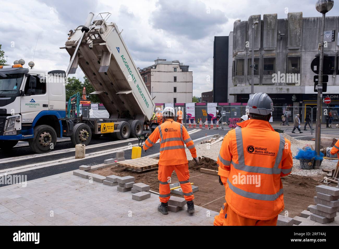 Ein Team von Arbeitern, die orangefarbene Overalls auf einer Baustelle tragen, arbeiten an der Fertigstellung der neuen Bahn für die Modernisierung des öffentlichen Nahverkehrssystems Midland Metro im Stadtzentrum entlang der Bull Street, gleich neben der Corporation Street am 20. Juli 2023 in Birmingham, Vereinigtes Königreich. Die neue Linie soll im Laufe des Jahres eröffnet werden. Die Midland Metro ist eine Straßenbahnlinie in der Grafschaft West Midlands, England, die zwischen den Städten Birmingham und Wolverhampton über die Städte West Bromwich und Wednesday verkehrt. Die Linie wird auf Straßen in städtischen Gebieten eingesetzt und wieder aufgefüllt Stockfoto