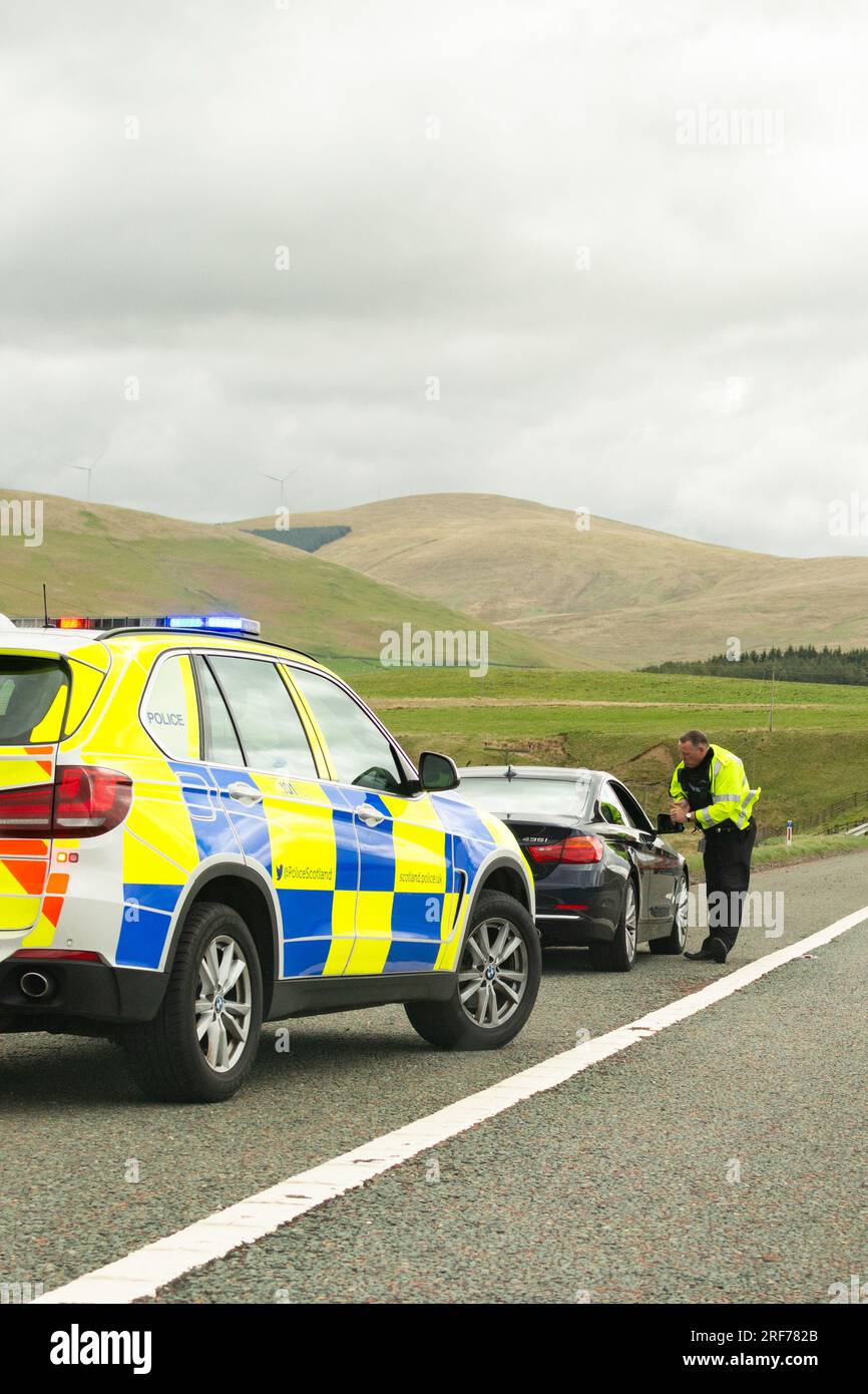 Ein Verkehrspolizist spricht mit dem Fahrer eines schwarzen bmw-Wagens, der auf der harten Schulter der Autobahn M74 in Schottland, Großbritannien, gehalten wurde Stockfoto