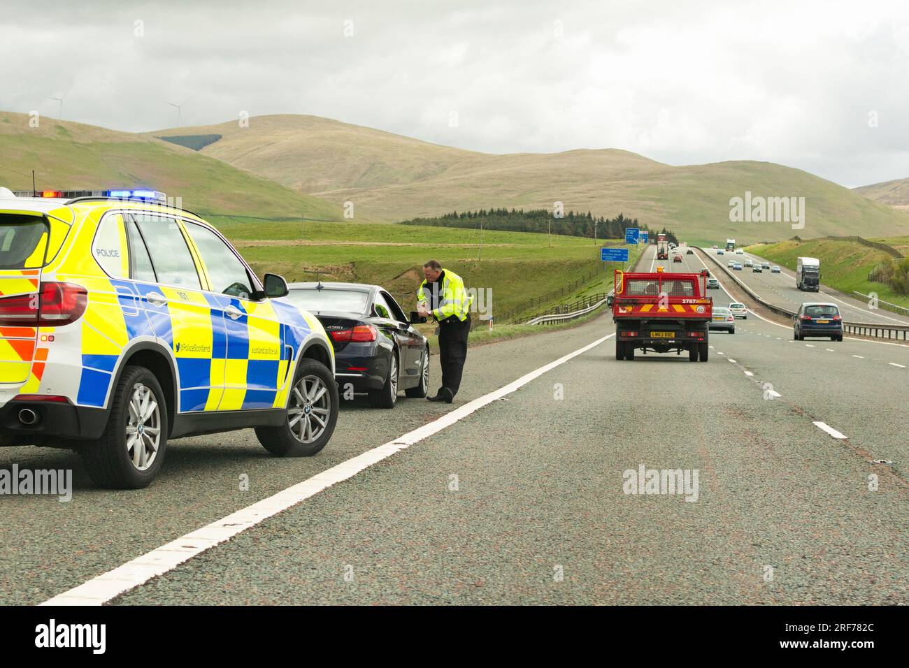 Ein Verkehrspolizist spricht mit dem Fahrer eines schwarzen bmw-Wagens, der auf der harten Schulter der Autobahn M74 in Schottland, Großbritannien, gehalten wurde Stockfoto