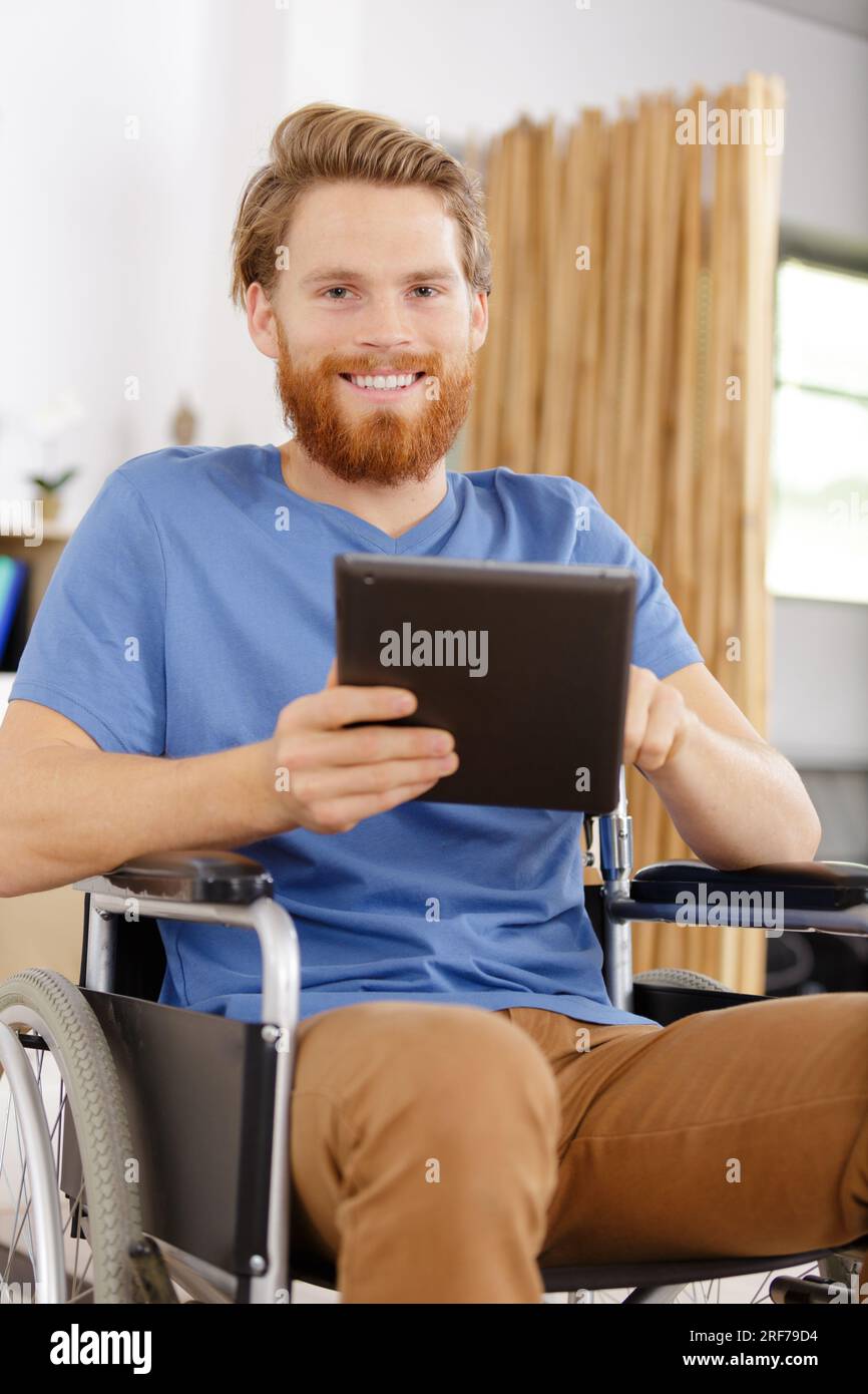 Glücklicher junger behinderter Mann, der es bemerkt, während er ein Tablet benutzt Stockfoto