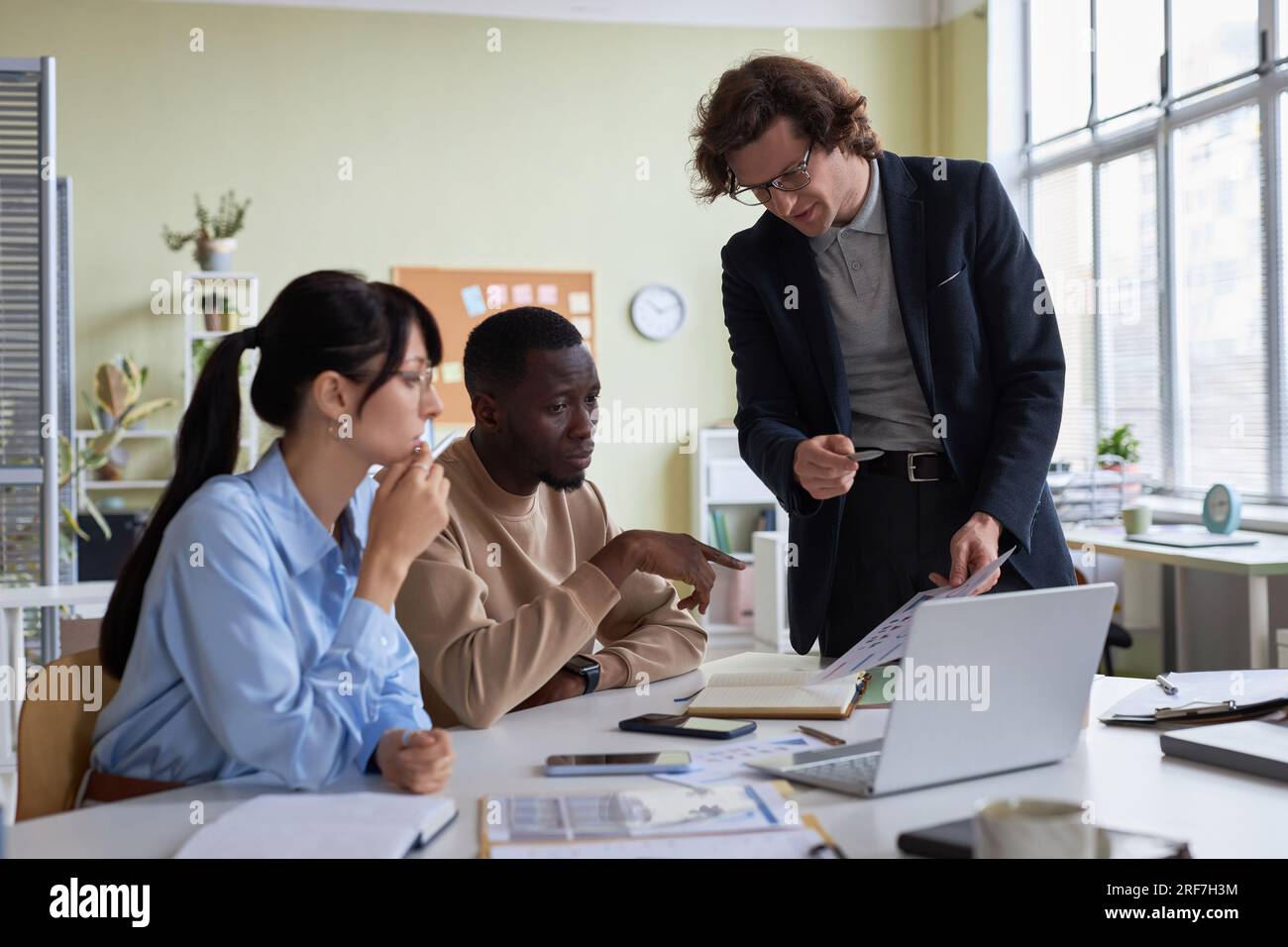 Ein vielseitiges junges Business-Team aus drei Mitarbeitern, die an einem Projekt im Büro zusammenarbeiten und Daten diskutieren Stockfoto