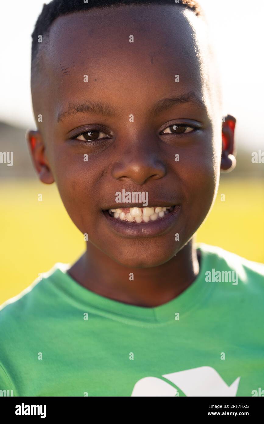 Ein afroamerikanischer Schuljunge, der ein Recycling-T-Shirt trägt und auf dem Sportplatz in der Grundschule lächelt Stockfoto