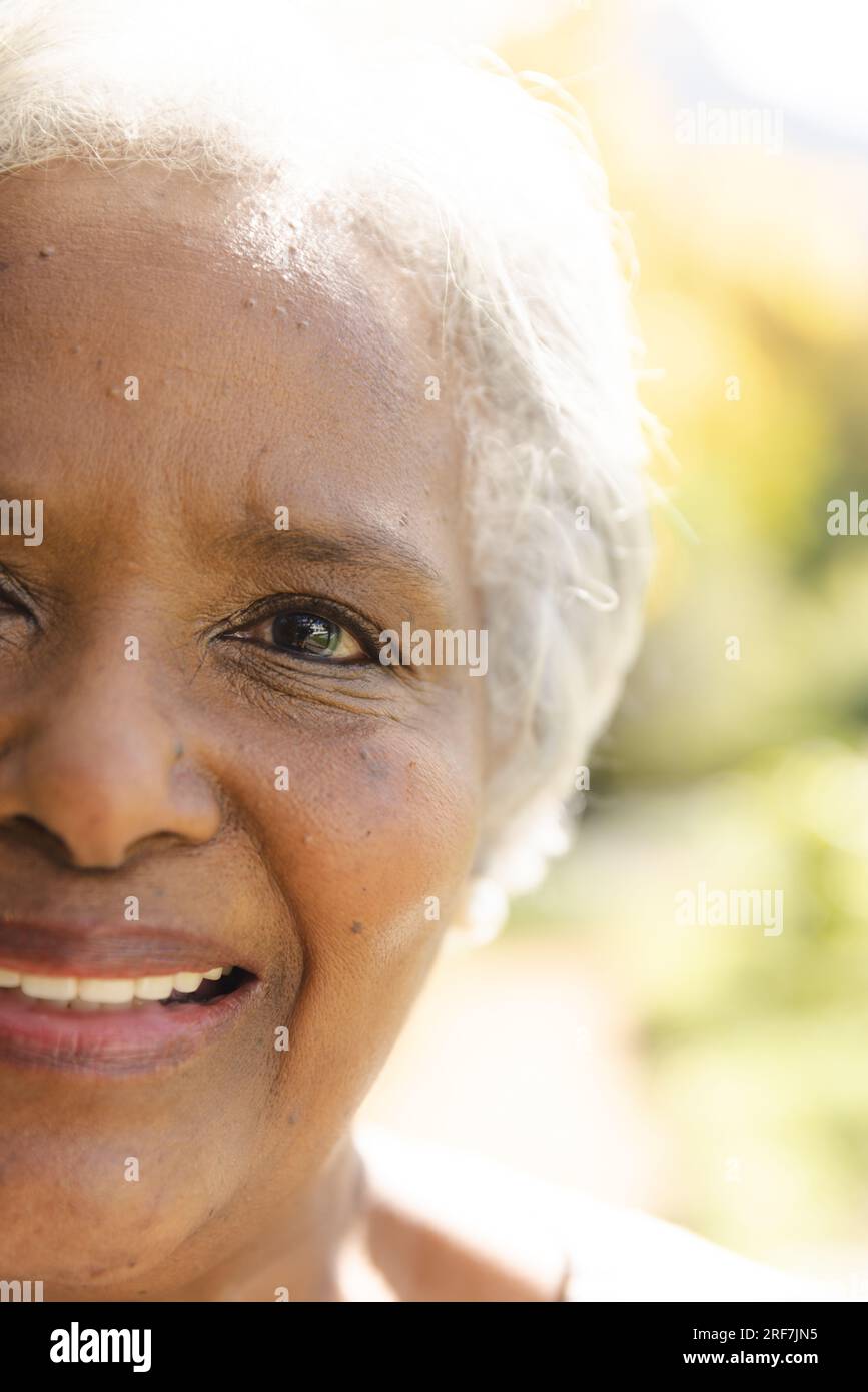 Ein halbes Porträt einer glücklichen älteren, birassischen Frau, die zu Hause im sonnigen Garten lächelt Stockfoto