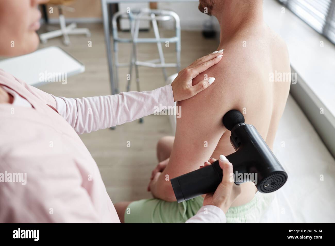 Arzt benutzt Massagegerät im medizinischen Verfahren mit dem Patienten, sie massiert seine Schmerzen zurück Stockfoto
