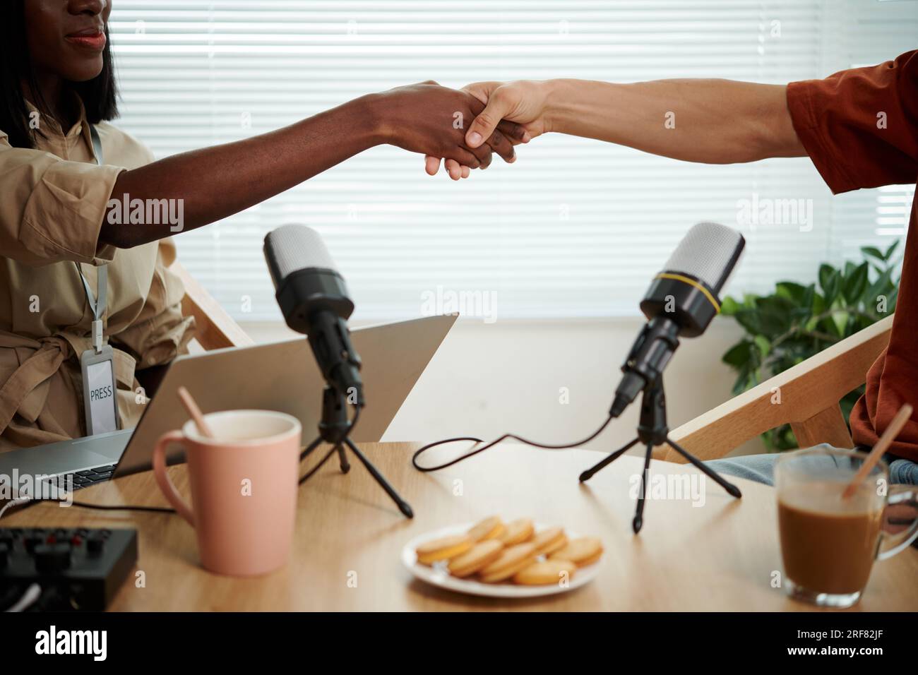Zugeschnittenes Bild von Podcaster und Gast, der die Hände über den Tisch schüttelt Stockfoto