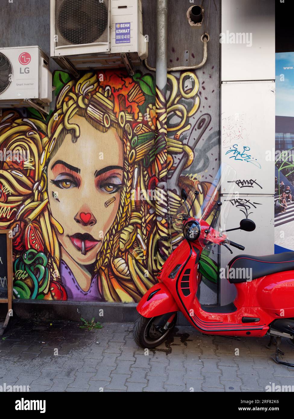 Roter Roller geparkt von Street Art einer Frau mit Locken im Haar, und Absaugventilator darüber, Stadt Sofia, Bulgarien. August 2023. Stockfoto
