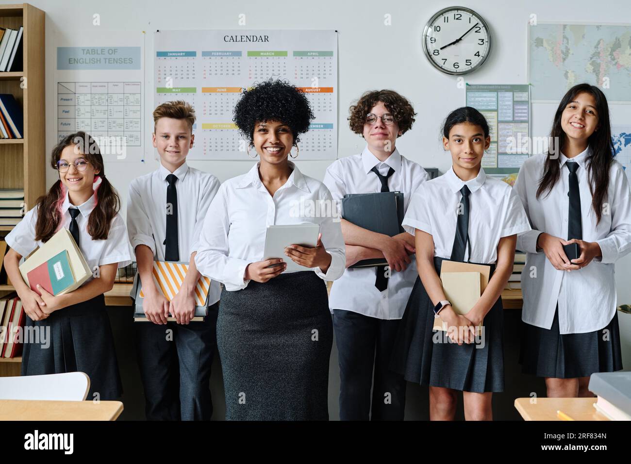 Porträt eines afroamerikanischen Lehrers, der zusammen mit den Schülern vor der Kamera lächelt, während sie im Klassenzimmer stehen Stockfoto