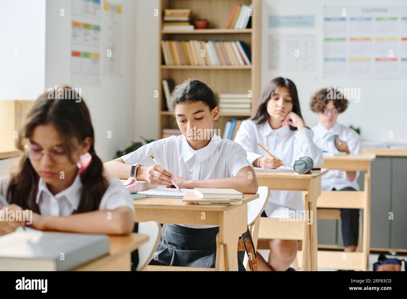 Gruppe von Schulkindern, die an Schreibtischen sitzen und sich während des Unterrichts Notizen in ihren Notizbüchern machen Stockfoto
