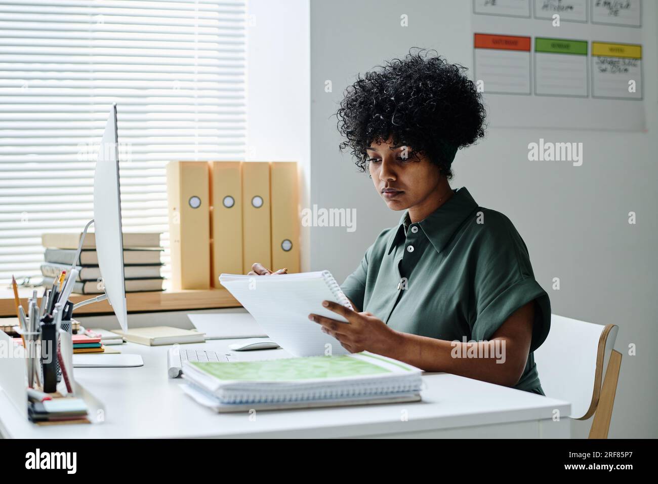 Lehrerin sitzt an ihrem Arbeitsplatz und bereitet sich auf den Unterricht im Klassenzimmer vor Stockfoto