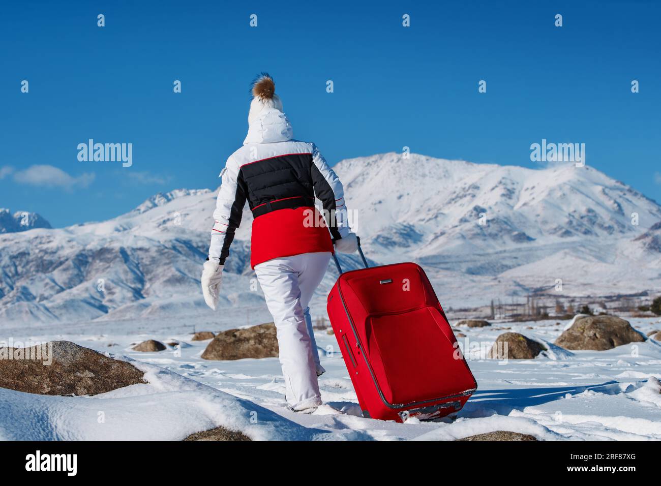 Junge Frau, die mit rotem Koffer im Hintergrund in den Winterbergen reist Stockfoto