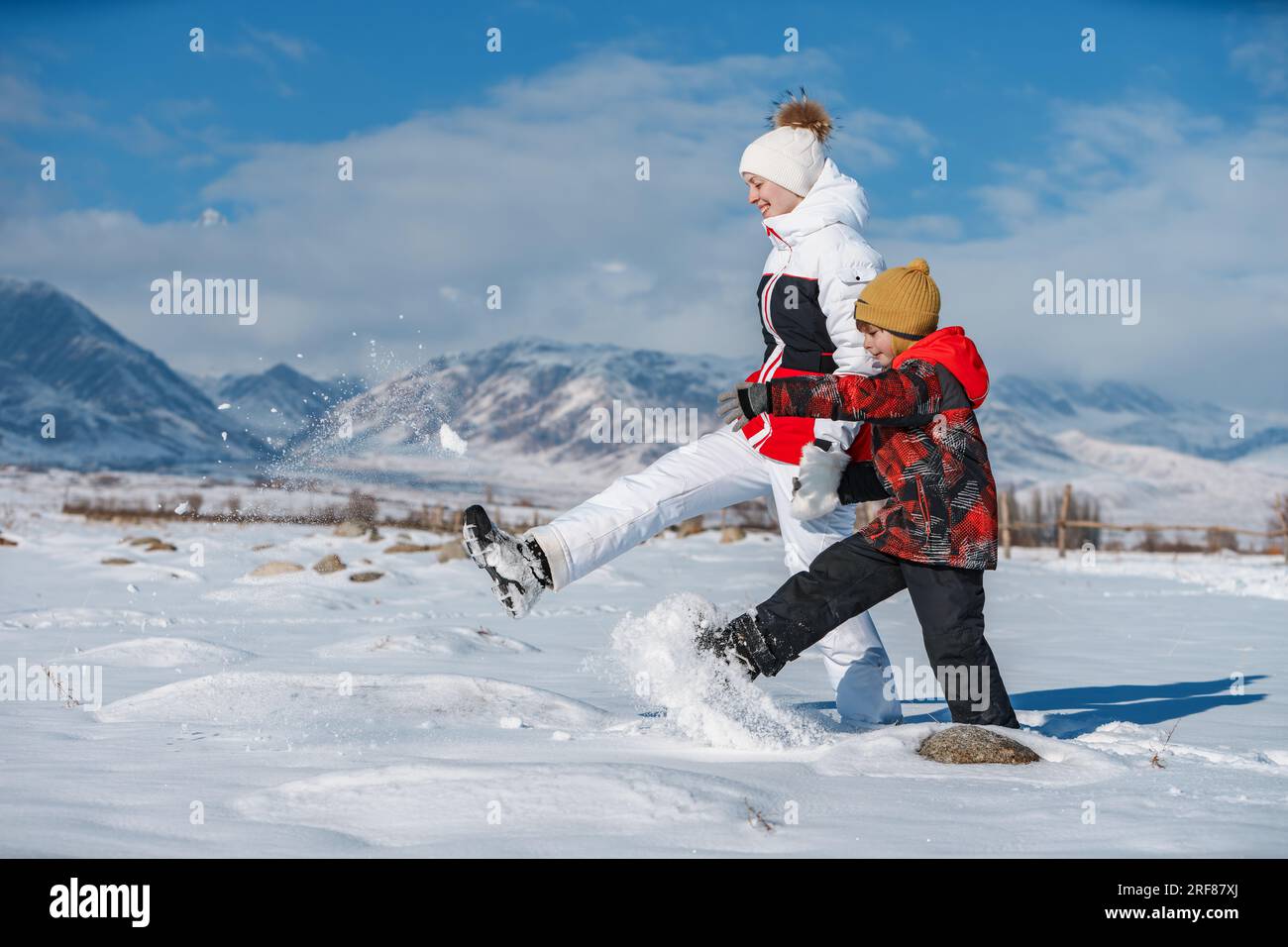 Junge Frau mit Kind, die an sonnigen Tagen im Schnee auf dem Hintergrund der Berge spaziert Stockfoto