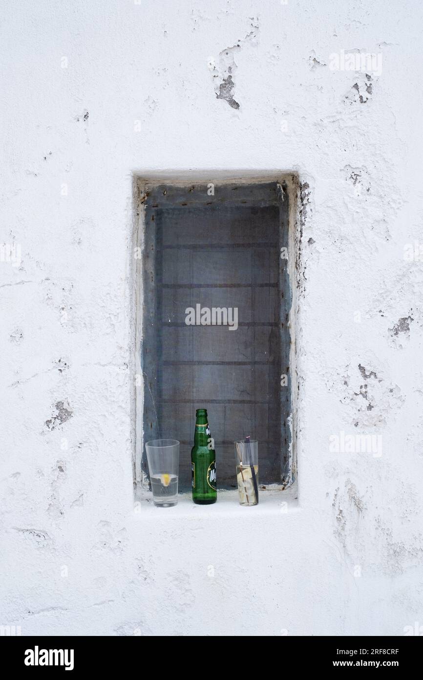 Ein überdachtes Fenster mit zwei Gläsern und einer leeren Flasche Bier, dort aufgegeben, Mykonos, Griechenland. Stockfoto