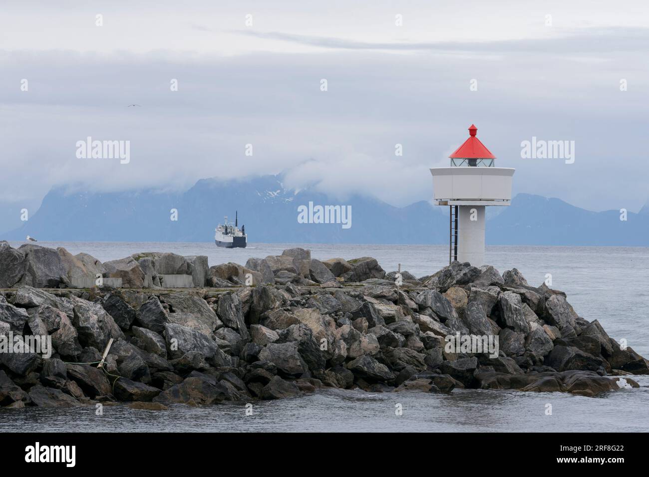 Kleiner Leuchtturm, am Ende einer Kaimauer, und die Fähre nach Gryllefjord, von einem Boot aus gesehen. Andenes, Andøya, Vesterålen-Archipel, Nordland, Norwegen Stockfoto