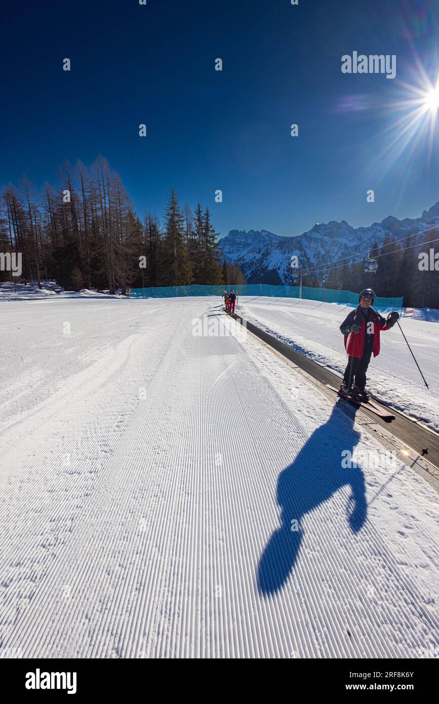 Falcade, Italien - 18. Februar 2023: Junger Mann auf einem Förderband für Skilifte, gemeinhin als magischer Teppich bekannt. Seine Skier liegen auf der beweglichen Oberfläche, r Stockfoto