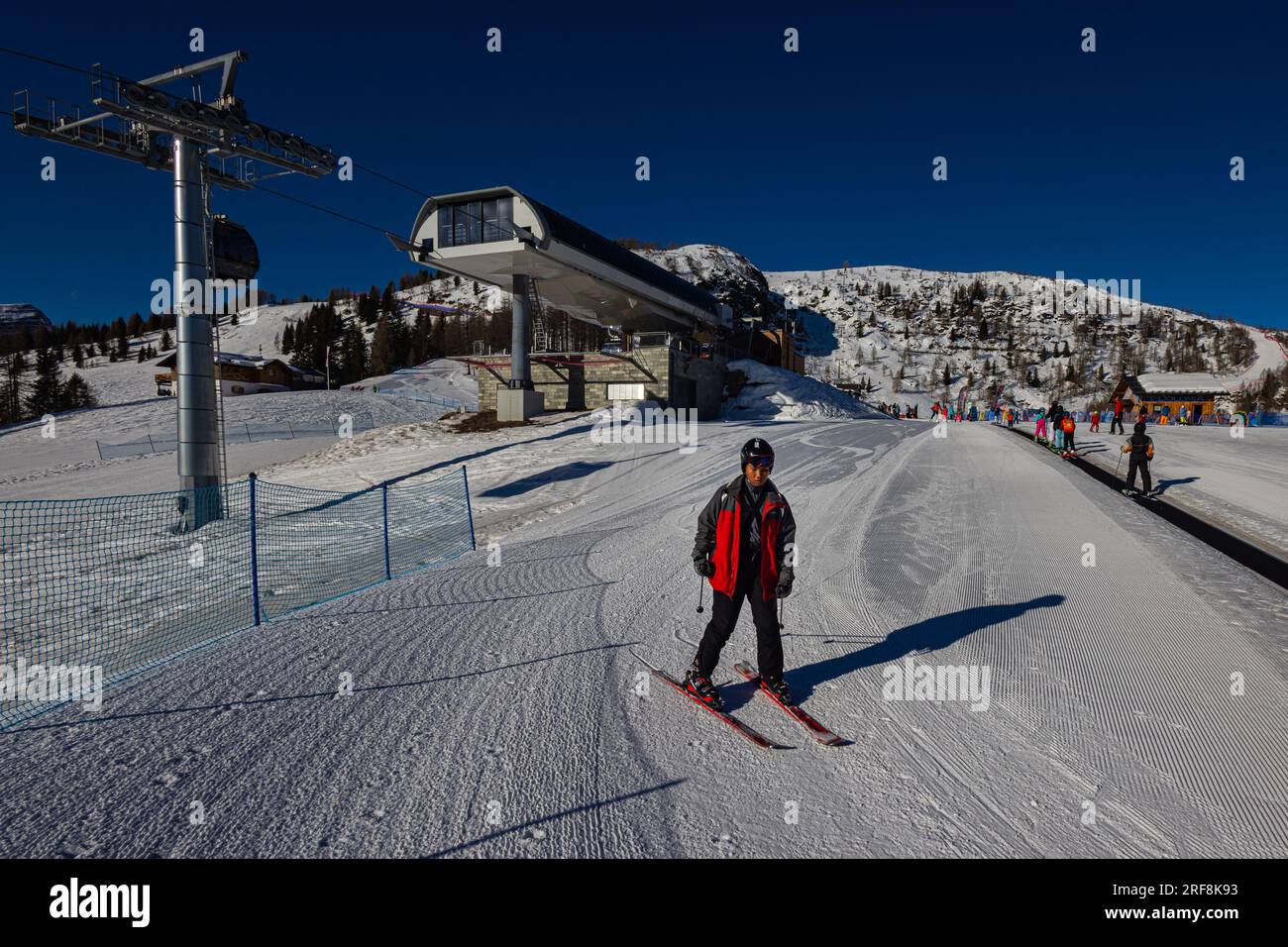 Falcade, Italien - 18. Februar 2023: Junger Mann fährt anmutig die Skipiste hinab, die sich in der Nähe eines Skilifts befindet. Sein Körper lehnt sich nach vorne, während er conf Stockfoto