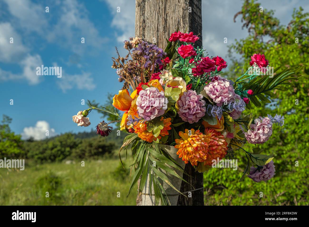 Holzkreuz mit bunten Stoffblumen an einer Kreuzung Stockfoto