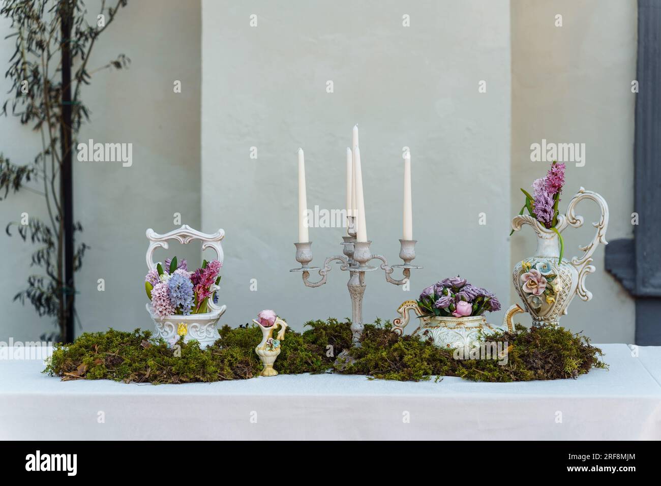 Dekorative Dekoration des Festtischs. Kerzenhalter mit Kerzen, Vasen mit Hyazinthen und anderen Blumen, grünes Moos auf einem Tisch, der mit einem bedeckt ist Stockfoto