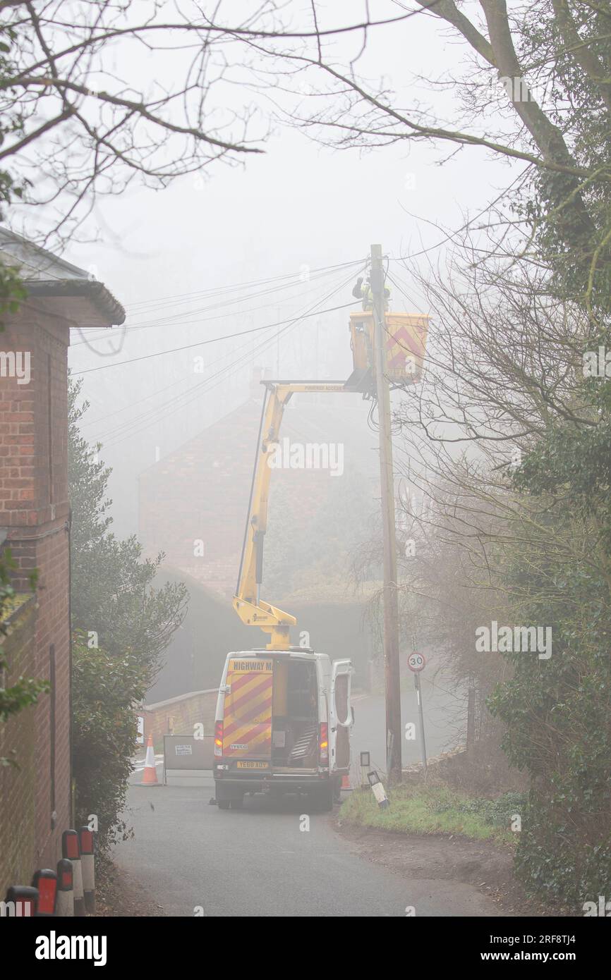 Telecom Engineer in einem Van Cherry Picker Lift, der an einem nebligen Tag auf einer britischen Landstraße an einem Telegrafenmast arbeitet. Stockfoto